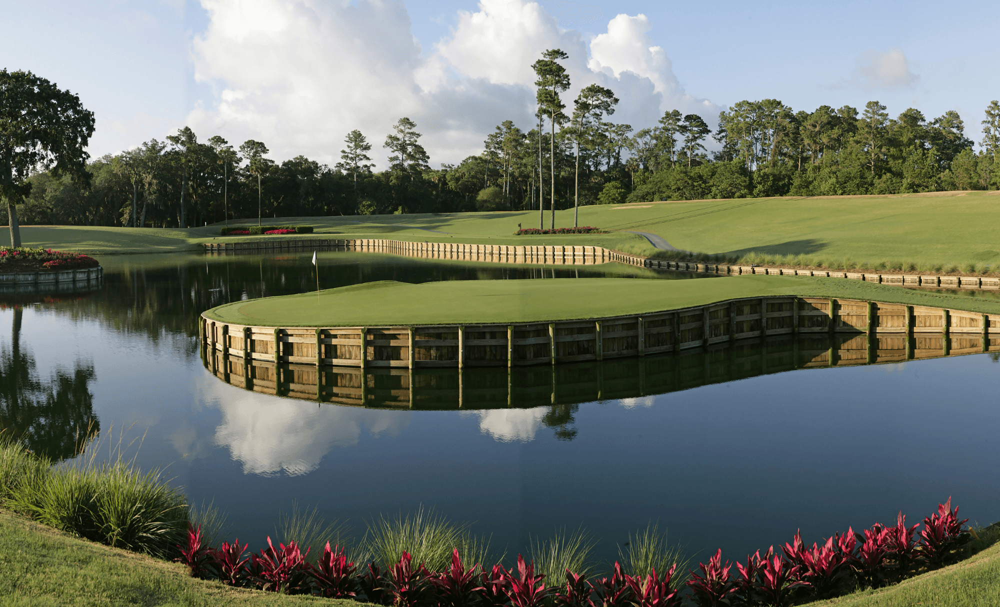 Aerial view of TPC Sawgrass 17th hole, famous island green surrounded by water, with lush fairway, bunkers, and trees under clear sky