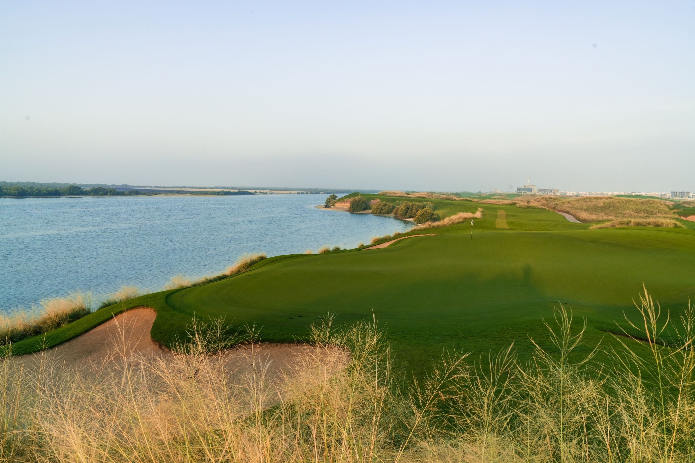 Aerial view of Yas Links golf course along the Dubai coastline, with green fairways, sandy bunkers, and blue water under a clear sky
