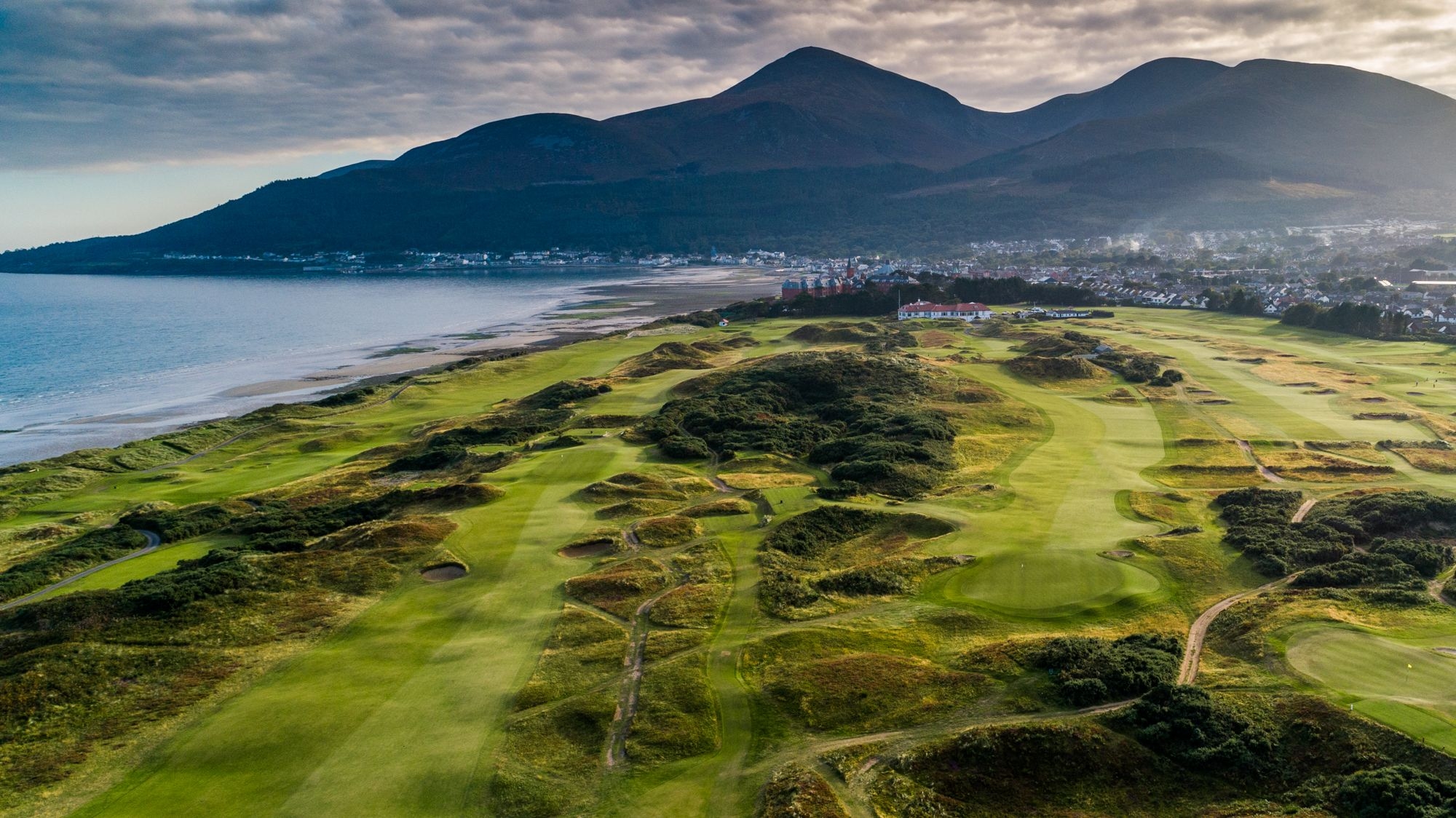 A scenic view of the Royal County Down golf course, showcasing its lush green fairways and the surrounding natural landscape.