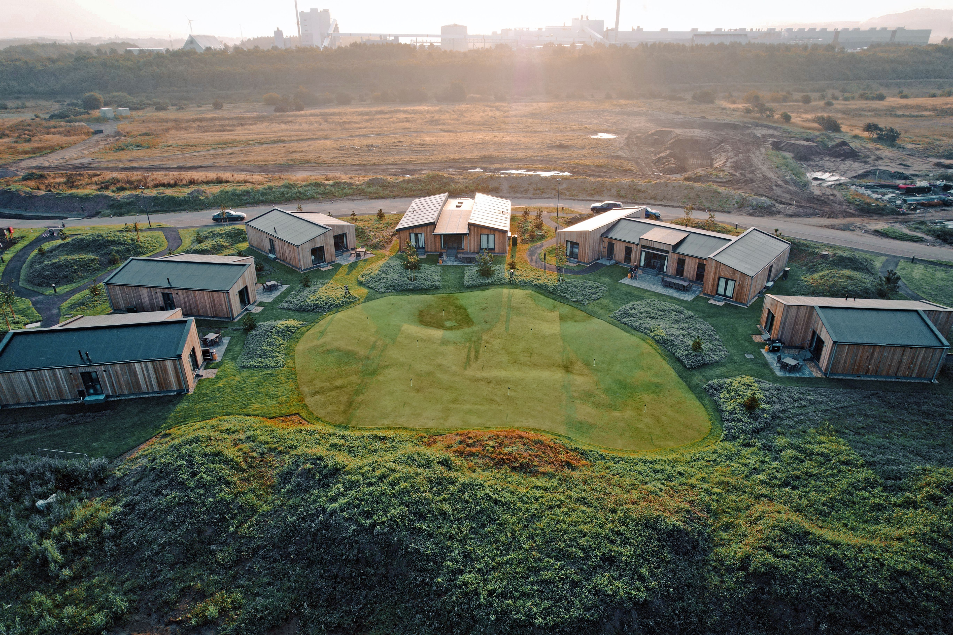 Modern Dundonald Links Lodges with wooden exteriors and large windows set beside a golf course under a bright, partly cloudy sky