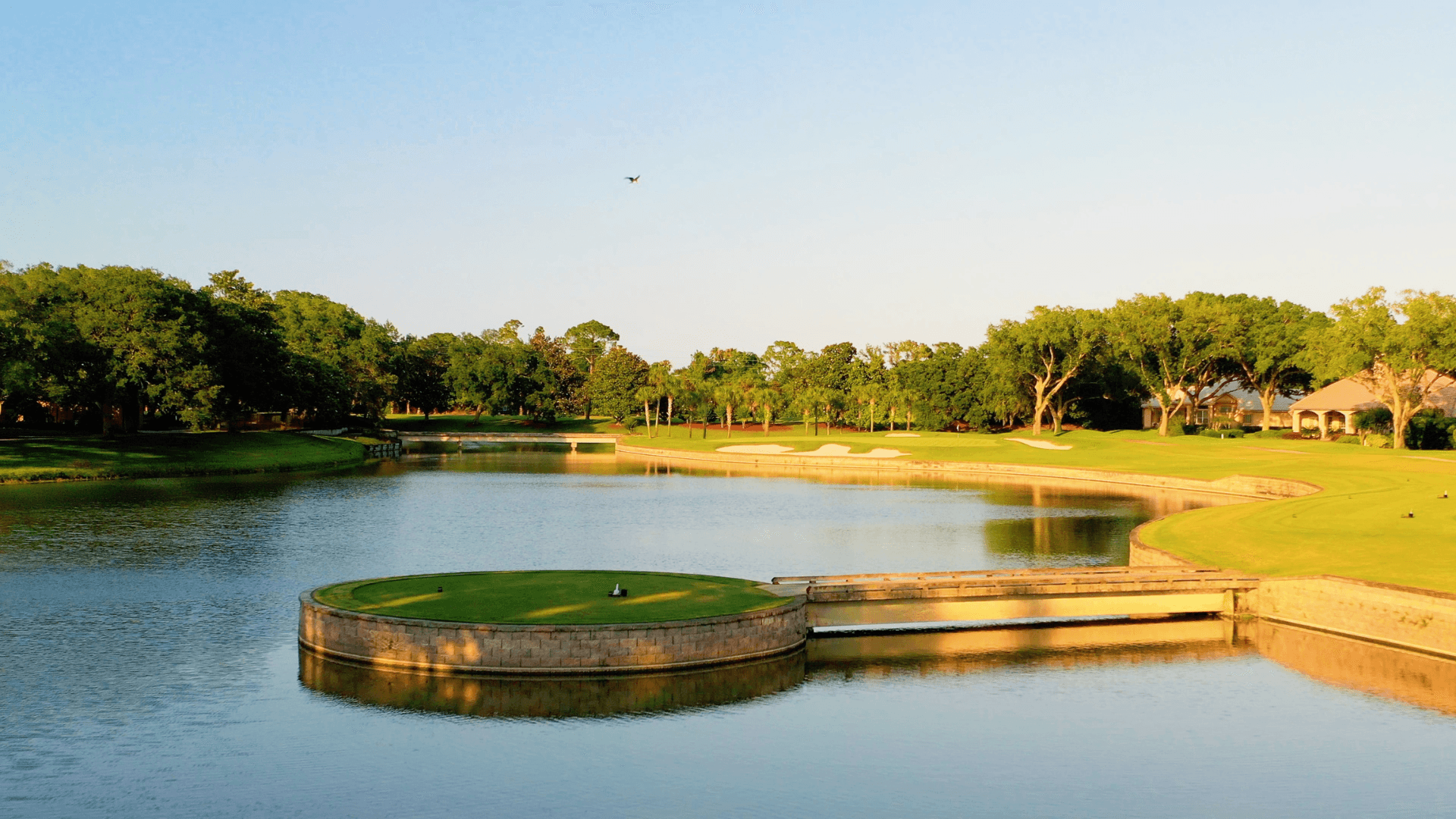 A lush green golf course on a small island surrounded by water, with fairways, trees, and manicured plantation-style landscaping.