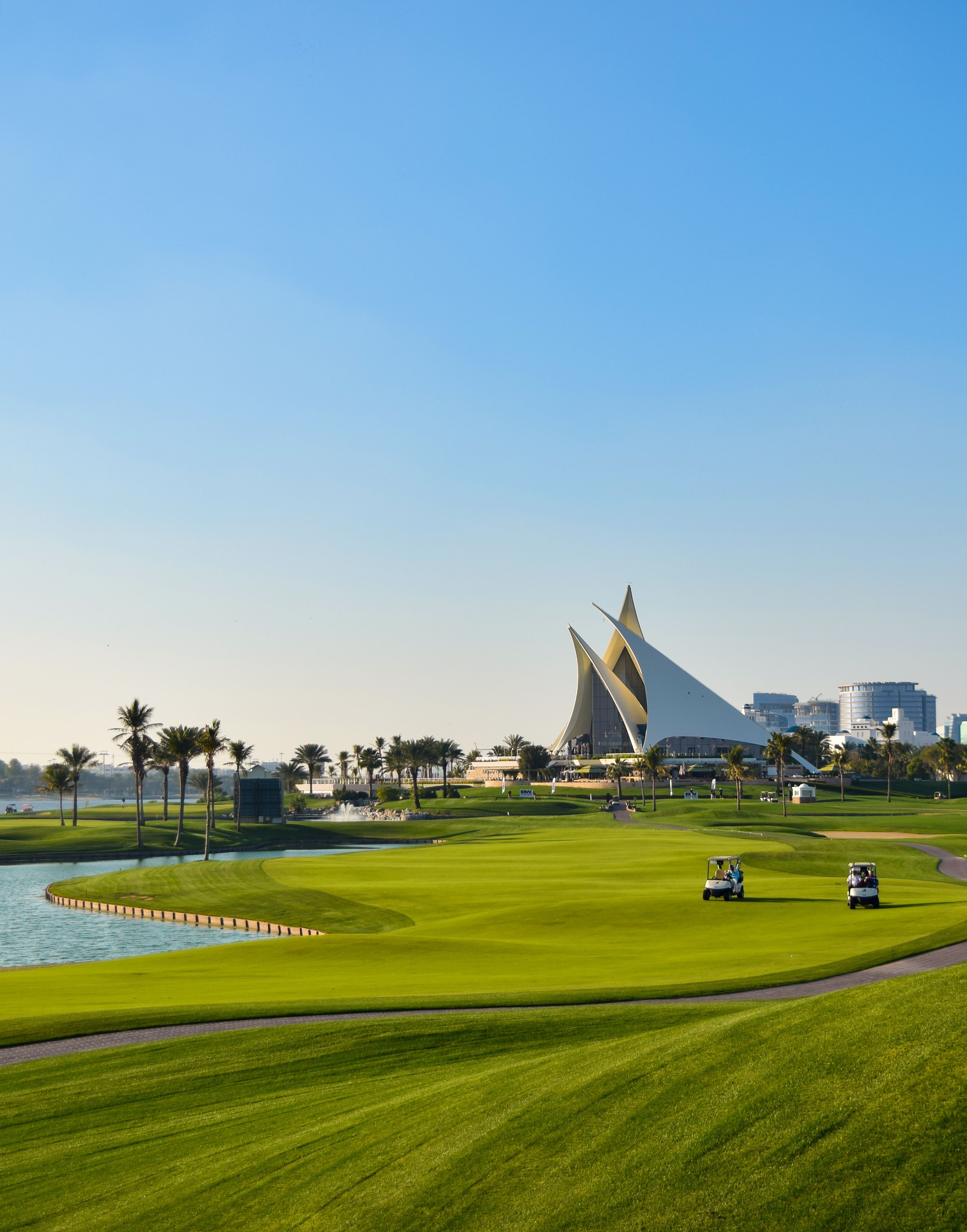 View of Dubai Creek Golf Course with lush green fairways, palm trees, and water features set against the modern Dubai skyline