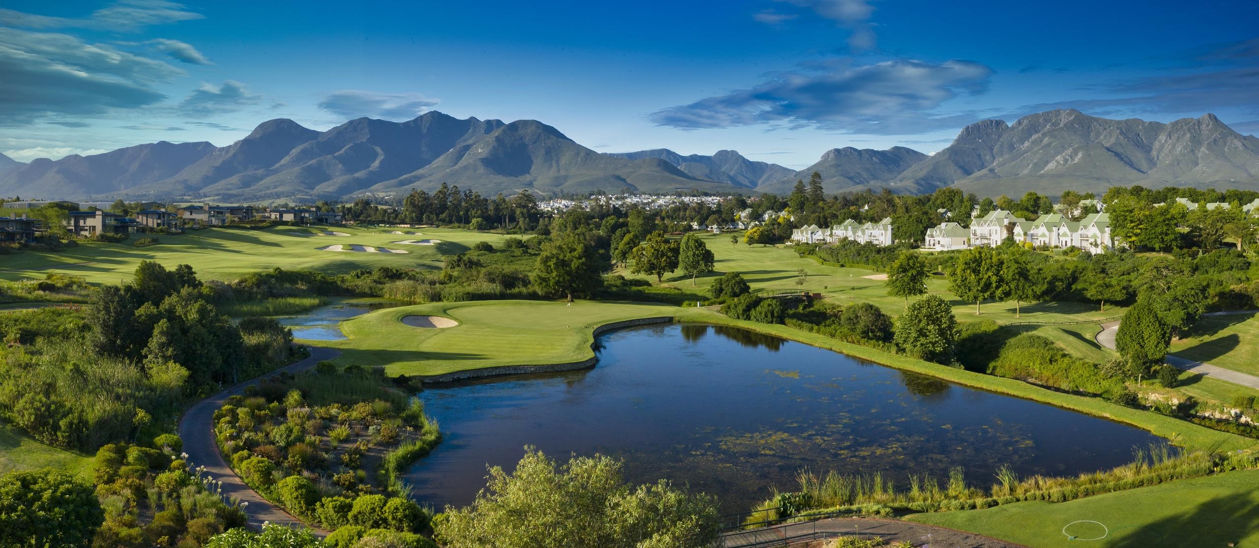 Panoramic view of Fancourt Montagu Golf Course, with lush fairways, trees and distant mountains beneath a blue sky.
