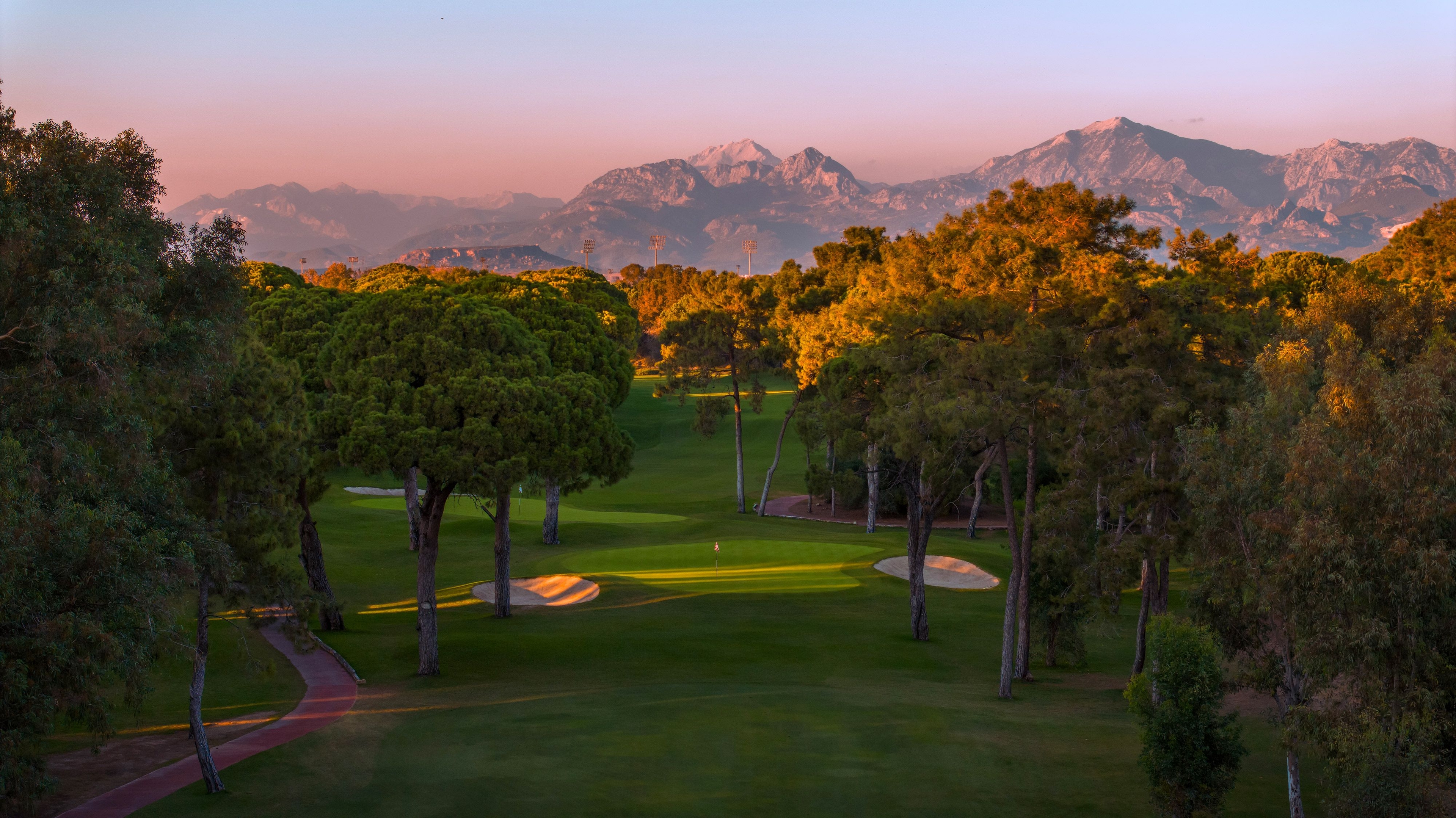 A wide view of the National Golf Course with manicured fairways, bright green grass, and trees lining the edges under a clear sky