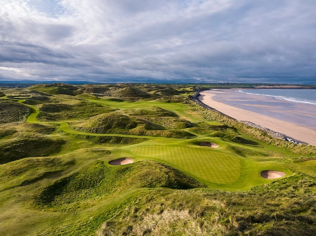 A wide view of Ballybunion Golf Course with rolling green fairways, rugged dunes, and the Atlantic Ocean visible along the dramatic coastline