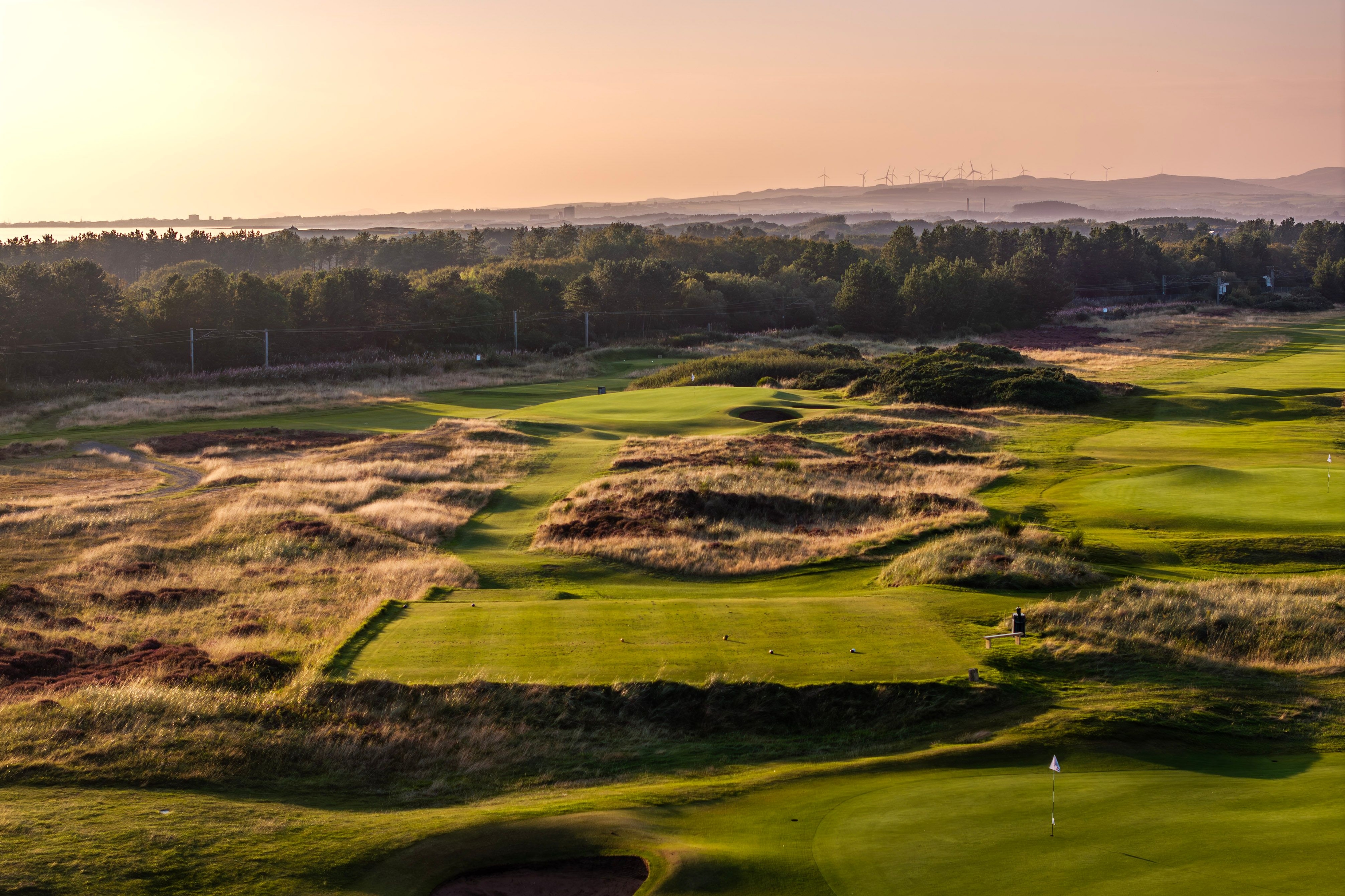 View across the Glasgow Gailes links golf course with rolling dunes, trimmed fairways, and distant clubhouse under a cloudy Scottish sky