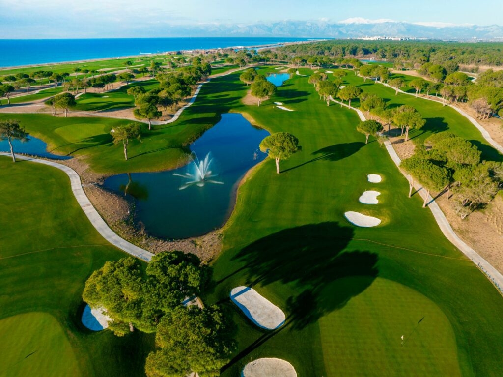 Wide view of Aspendos Golf Course with manicured fairways, greens, and surrounding trees under a clear sky